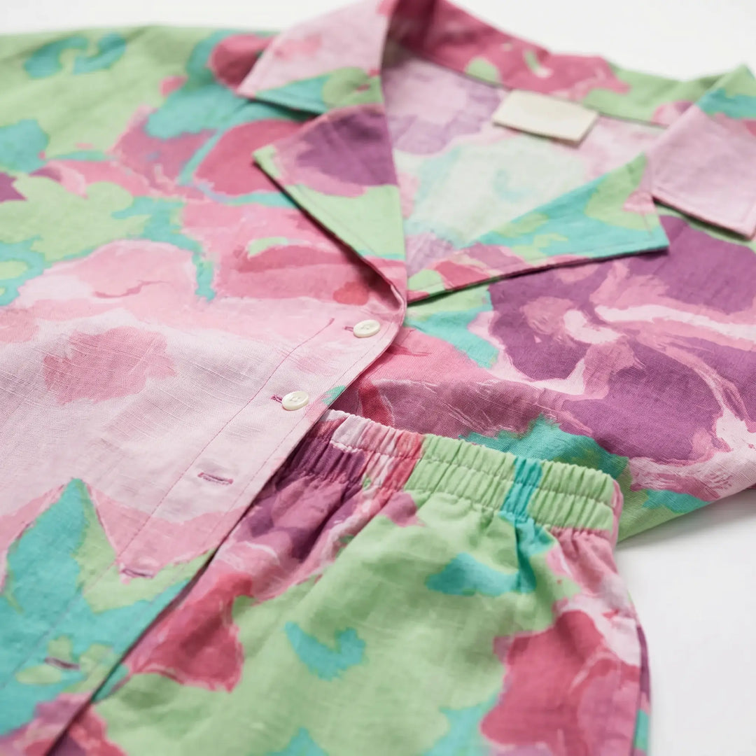 Close-up detail of a two-piece loungewear set featuring an abstract floral print in vibrant fuchsia, mint green, and magenta on a white background, showcasing fabric texture and button detail.