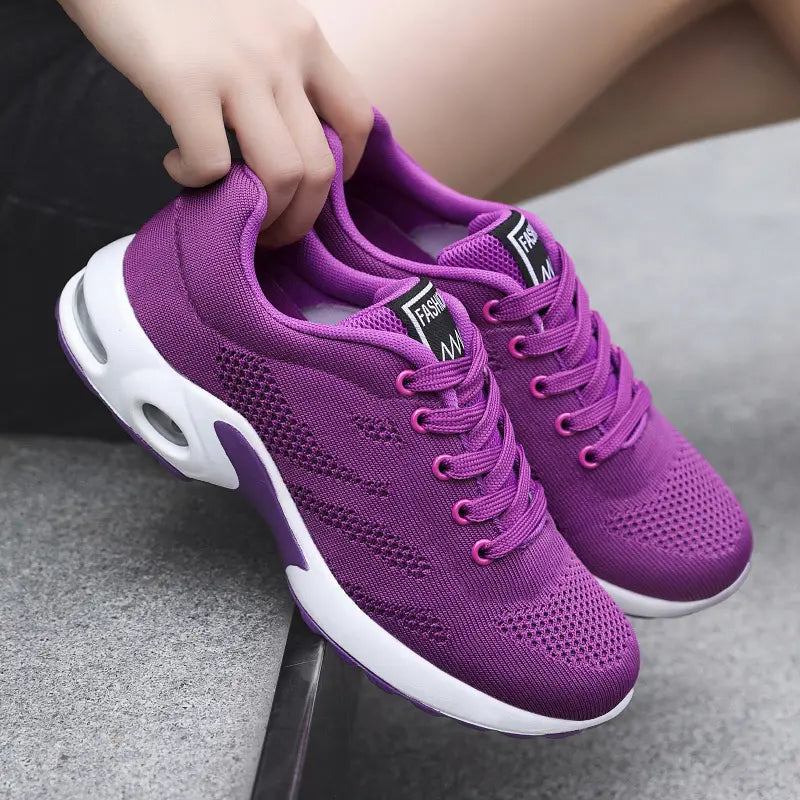 Aerion vibrant violet knit trainers with bright pink laces and white air-cushioned soles, shown from a three-quarter angle. The shoe features breathable mesh and a decorative tongue label.