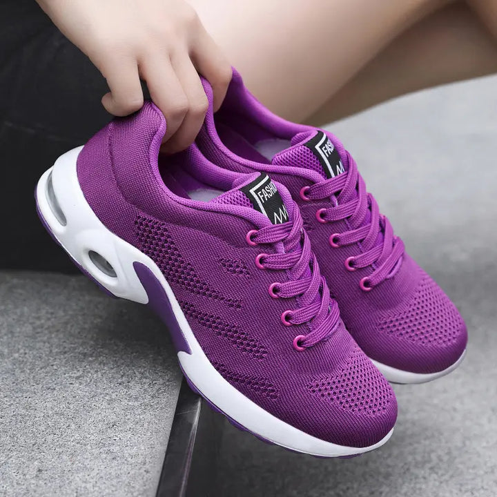 Aerion vibrant violet knit trainers with bright pink laces and white air-cushioned soles, shown from a three-quarter angle. The shoe features breathable mesh and a decorative tongue label.