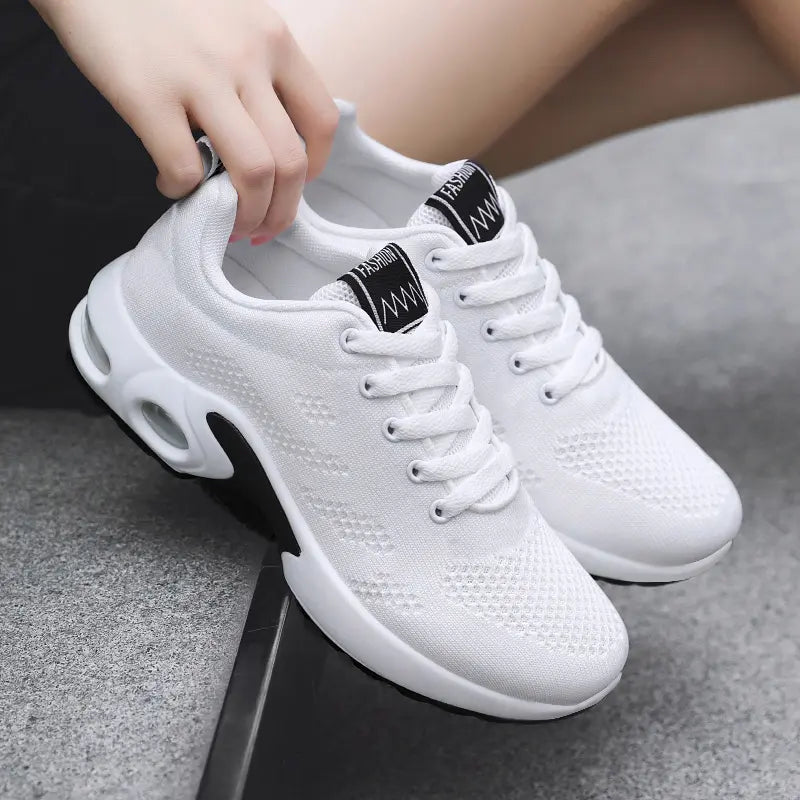 Aerion women's white breathable knit trainers with bright pink laces, showcasing the air cushioning sole and textured mesh upper, held by a hand.