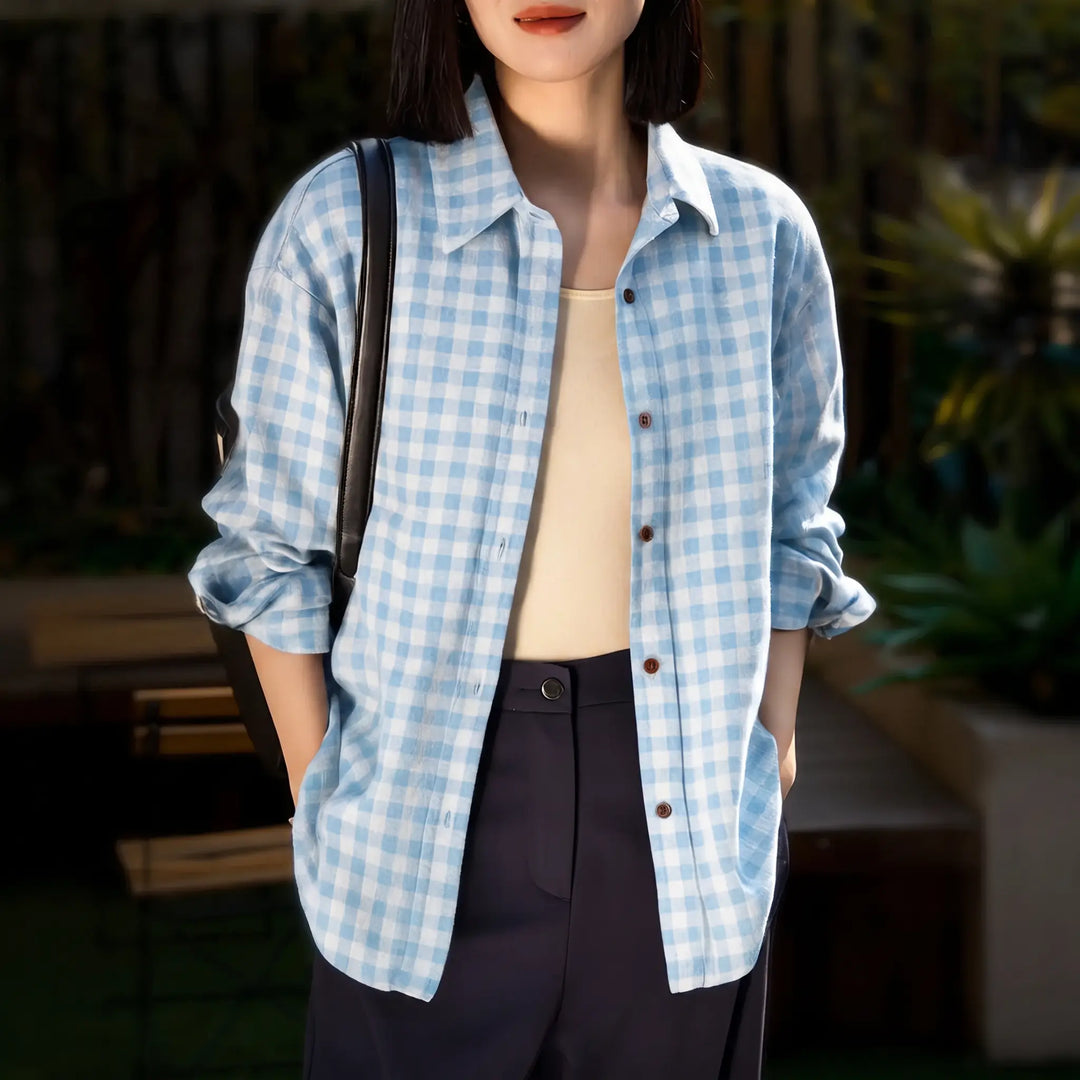 A woman wearing a relaxed-fit, light blue and white plaid brushed cotton shirt with a POLO collar and buttoned cuffs, styled over a beige tank top and dark trousers.
