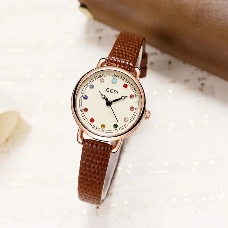 Aethel quartz watch with a rose gold tone case, cream dial, and 12 colourful gemstone-inspired markers, paired with a brown pebbled leather strap.
