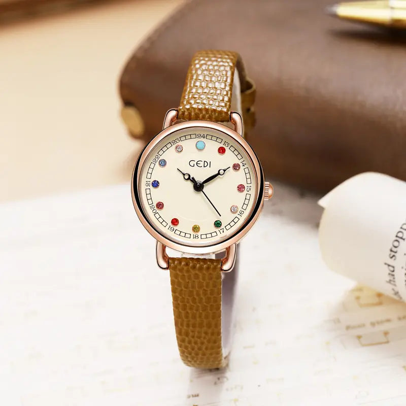Front view of a women's Aethel quartz watch with a rose gold case, cream dial, and colourful gemstone-inspired markers, paired with a brown embossed leather strap. The watch features slim black hands and a small crown.