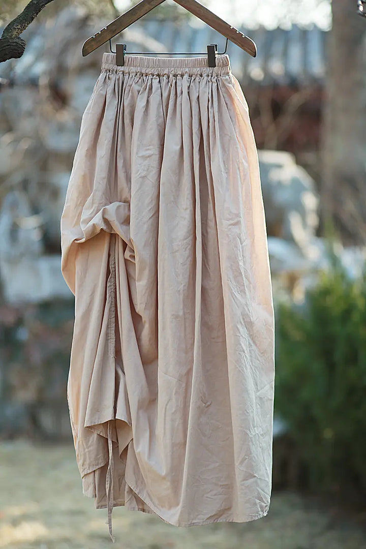 Avant-garde asymmetrical draped maxi skirt in soft off-white cotton, featuring an elasticated waistband and adjustable drawstring hem for volume control.