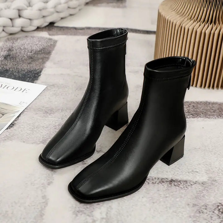Axorian black faux leather ankle boots with a sharp square toe and a 4.5cm geometric block heel, featuring a convenient rear zipper closure.