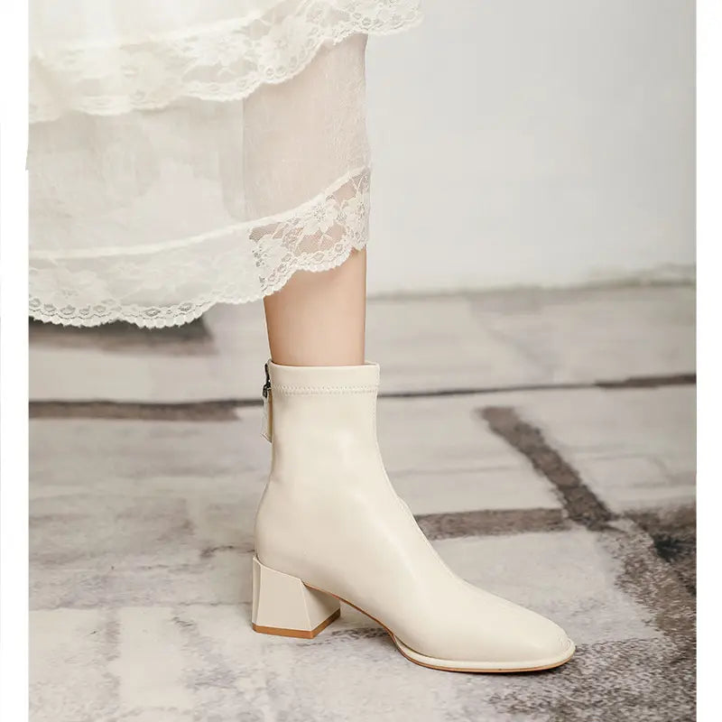 Cream-colored Axorian ankle boots with a square toe and block heel, shown on a model&