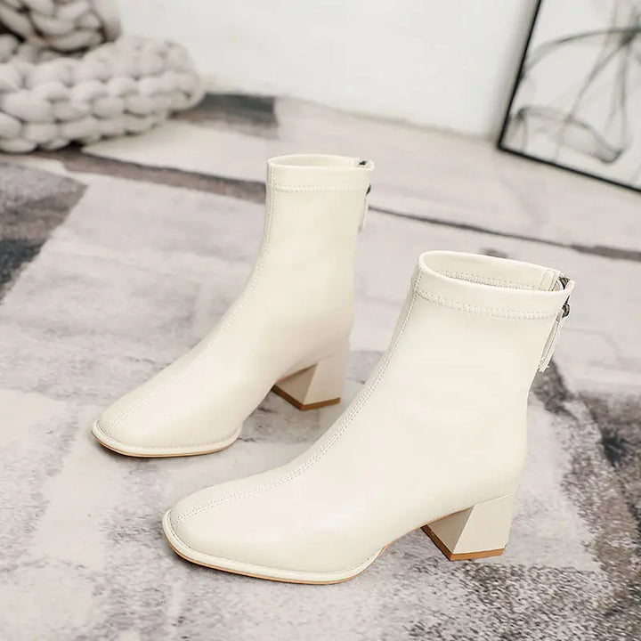 Axorian chic cream faux leather ankle boots featuring a sharp square toe, comfortable block heel, and convenient rear zipper closure, shown in a three-quarter view.