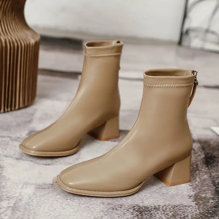 Pair of Axorian taupe faux leather ankle boots with a square toe, chunky block heel, and rear zipper closure, shown at a three-quarter angle.