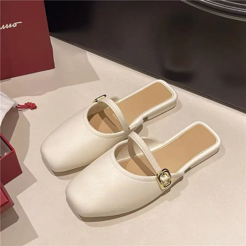 Pair of Azoria ivory matte faux leather square-toe mules with a slender strap and gold-tone square buckle, shown from a three-quarter angle on a studio surface.