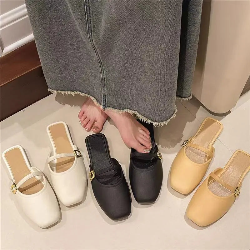 Azoria ivory, black, and beige matte faux leather square-toe mules with gold buckle straps, shown styled on feet.