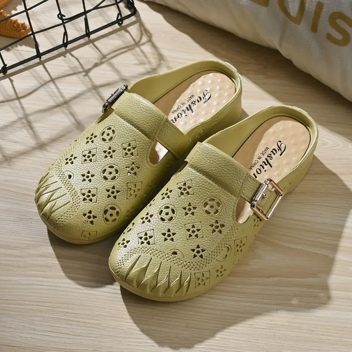 Pair of light khaki Azova textured synthetic mules with embossed geometric pattern, round pleated toe, and adjustable gold buckle strap, presented on a wooden surface.