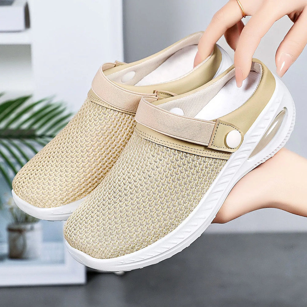 Light beige breathable mesh clogs with air cushion sole and adjustable strap, shown held by hands against a soft-focus background.