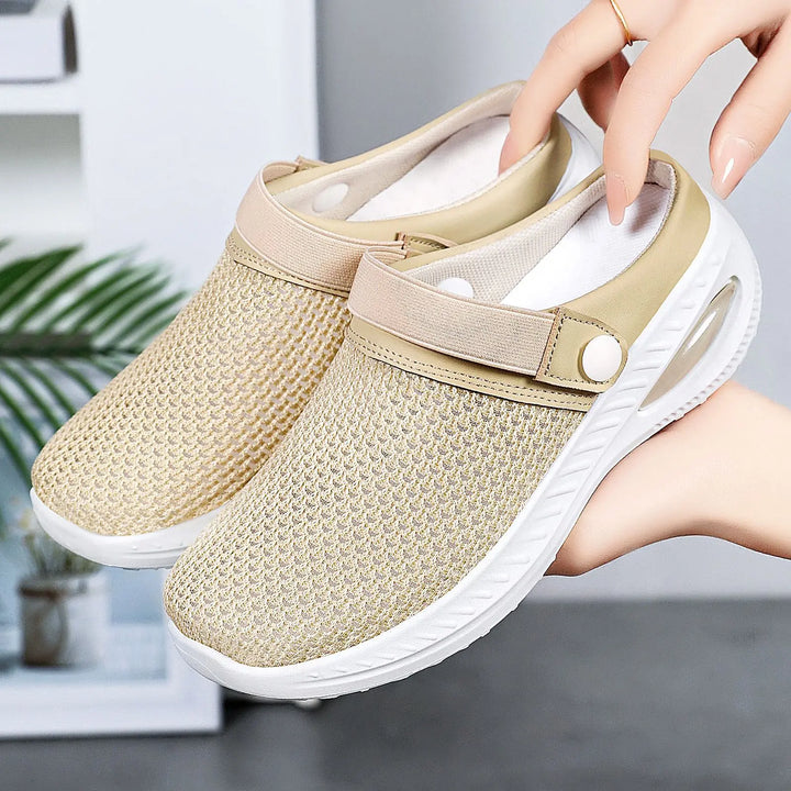 Light beige breathable mesh clogs with air cushion sole and adjustable strap, shown held by hands against a soft-focus background.