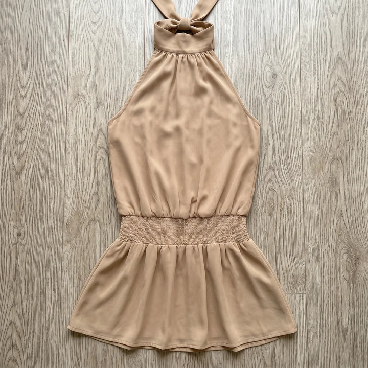Soft beige polyester blend halter neck mini dress with a shirred elastic waistband and a flattering A-line skirt, laid flat for display.