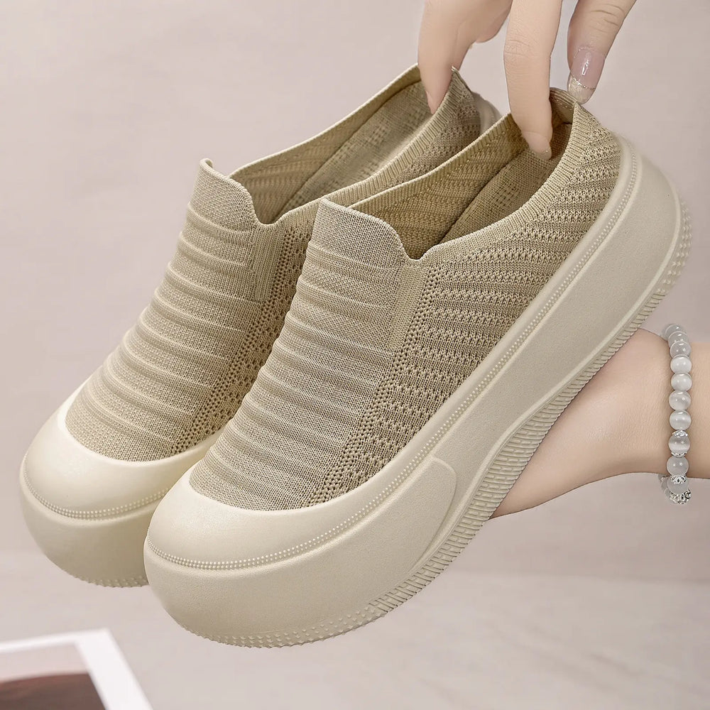 Beige knit slip-on platform mules with a round closed toe, held up by hands, showcasing their chunky light beige sole and fine ribbed upper.