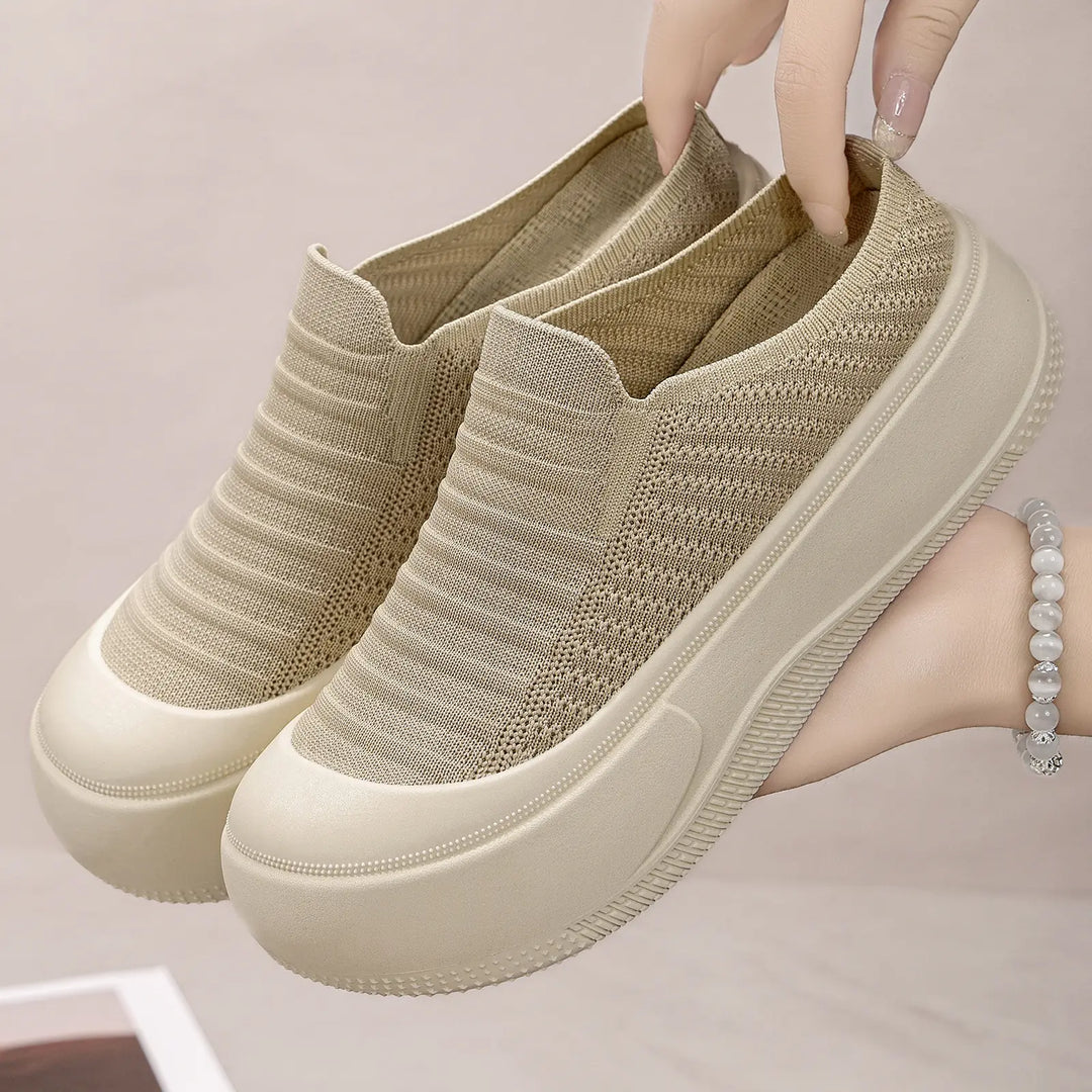 Beige knit slip-on platform mules with a round closed toe, held up by hands, showcasing their chunky light beige sole and fine ribbed upper.
