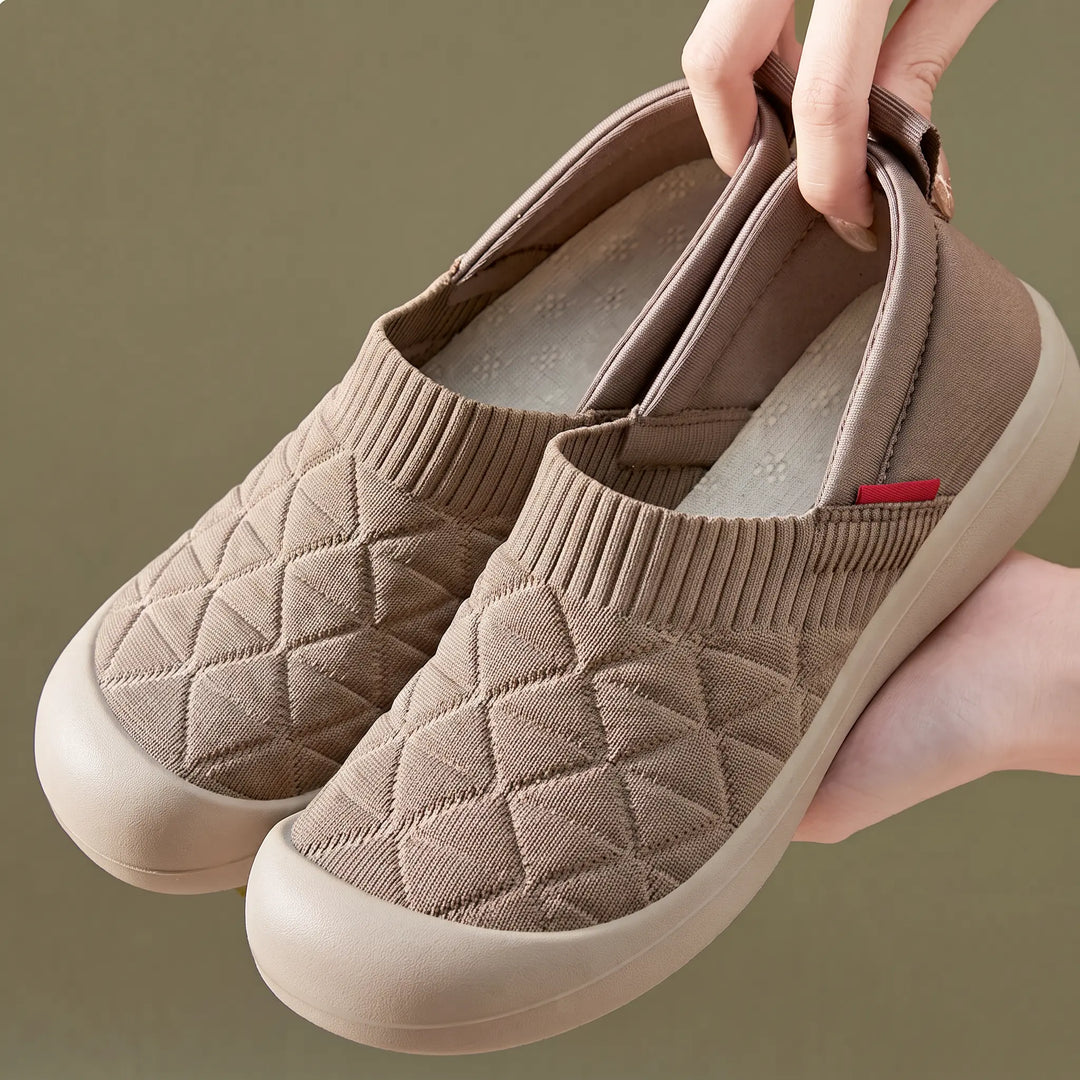 A pair of light beige knit slip-on sneakers with a diamond quilted pattern, featuring a red &