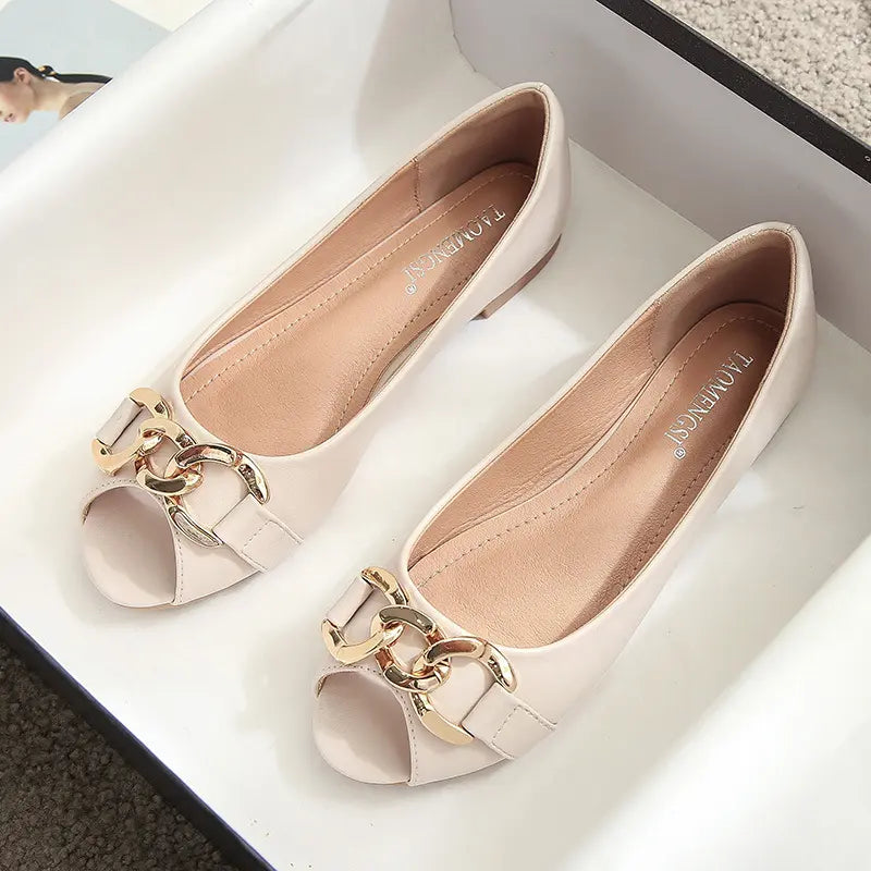 A pair of light beige peep-toe flat shoes with a gold-tone chain link embellishment across the vamp and a flat heel.