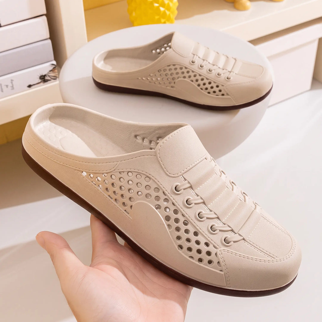 Close-up of a light beige perforated slip-on mule clog, showing the "FASHION" and "VIP" text detail on the side and faux lace-up design. The shoe has a dark brown sole and is viewed from a three-quarter angle.