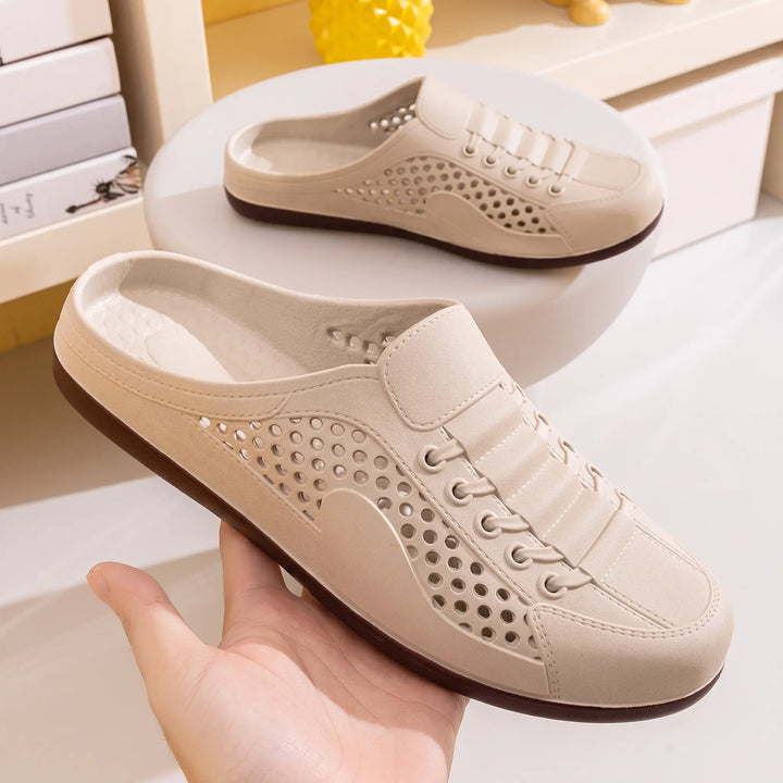 Close-up of a light beige perforated slip-on mule clog, showing the "FASHION" and "VIP" text detail on the side and faux lace-up design. The shoe has a dark brown sole and is viewed from a three-quarter angle.