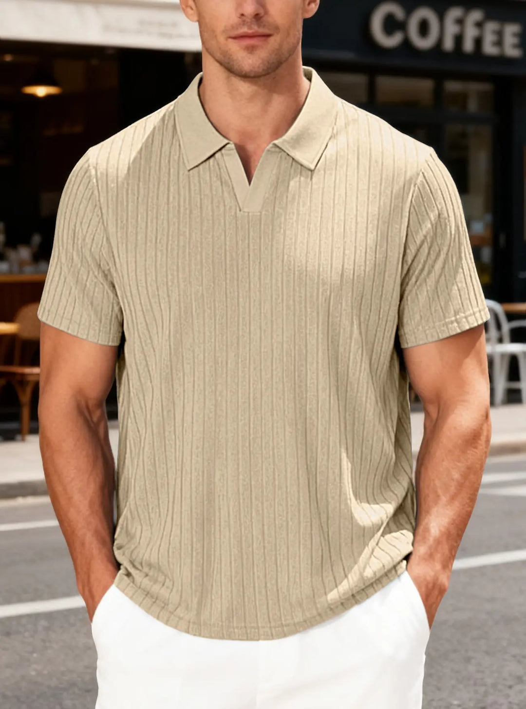 Man wearing a beige textured knit short-sleeved polo shirt with a relaxed fit and V-neck collar, set against an urban cafe background.