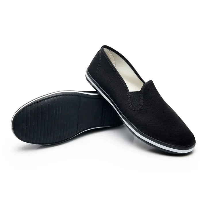Black canvas slip-on loafers with a white sole stripe and visible tread pattern on the rubber sole, shown from a three-quarter angle.