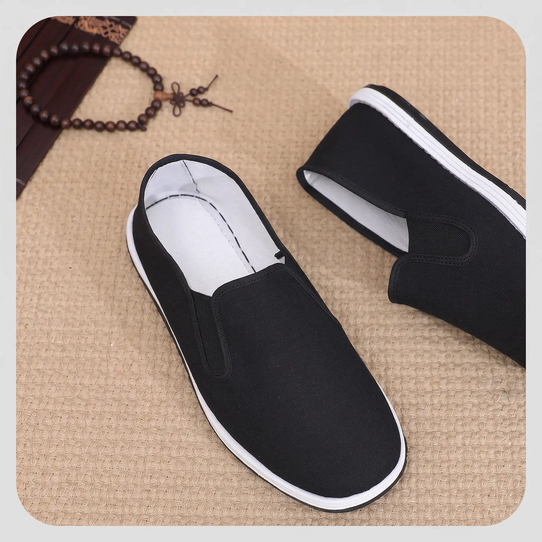 Black canvas slip-on loafers for men, featuring a white rubber sole stripe and elasticated side panels for easy wear. These breathable shoes offer comfort for everyday use.