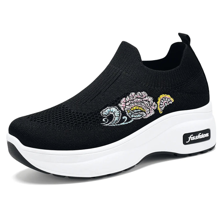 Black slip-on knit sneakers featuring a vibrant embroidered floral motif on the side and a thick white platform sole with a "fashion" logo detail.