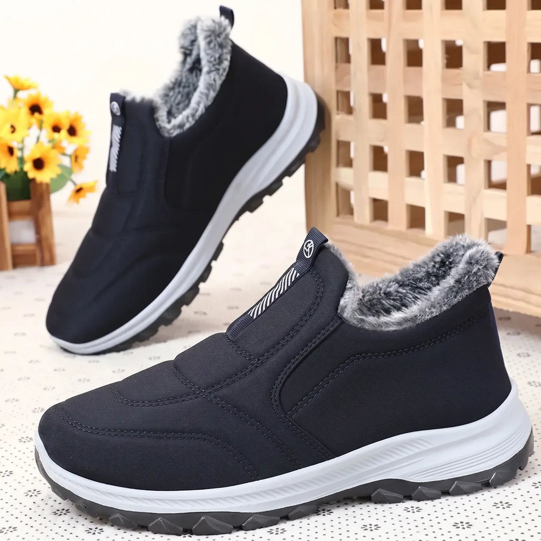 Pair of black quilted slip-on winter boots with grey faux fur lining, white midsole, and textured dark sole, shown from a three-quarter angle.