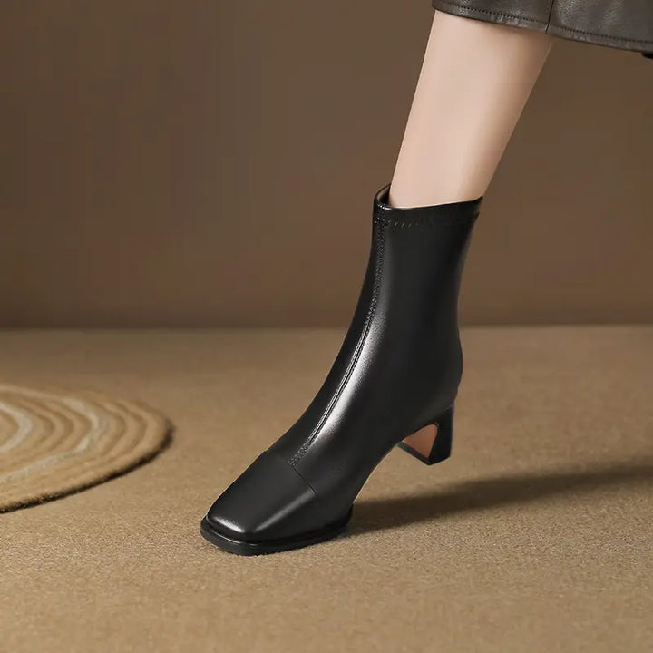 Black faux leather ankle boots with a square toe and block heel, worn by a model showing the mid-calf shaft in a subtle lifestyle setting.