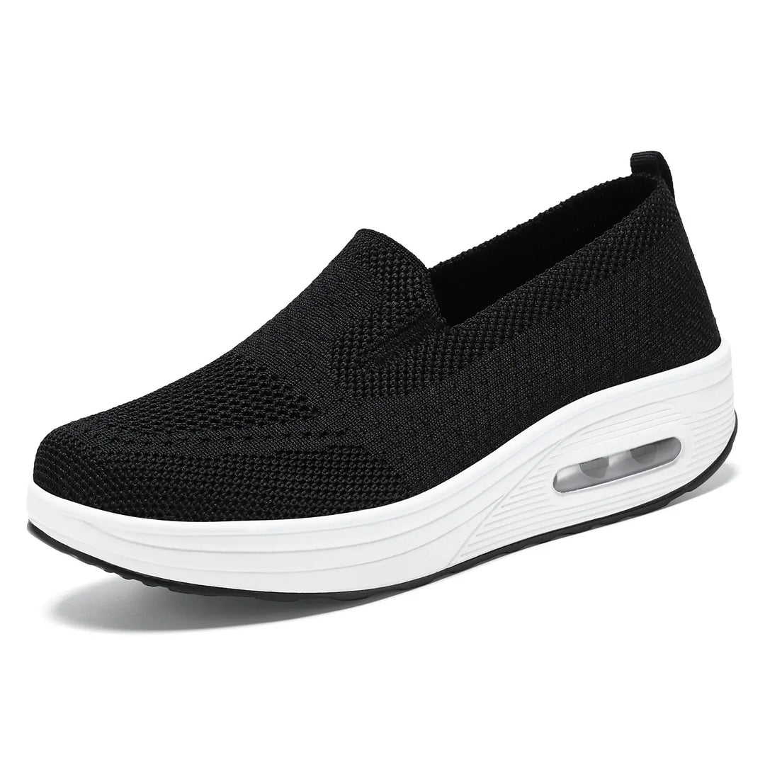 Black breathable knit slip-on sneaker with a white platform sole featuring a visible air cushion in the heel, presented at a side angle on a clean white background.