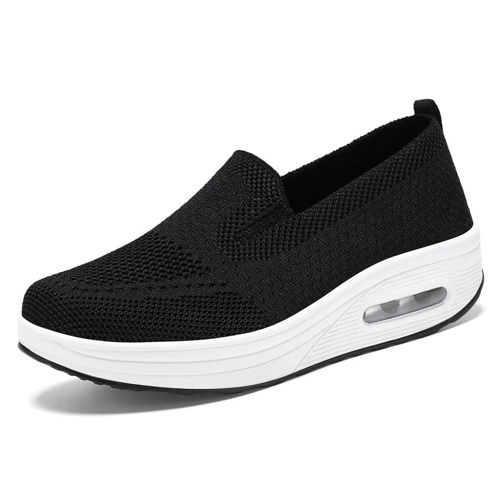 Black breathable knit slip-on sneaker with a white platform sole featuring a visible air cushion in the heel, presented at a side angle on a clean white background.