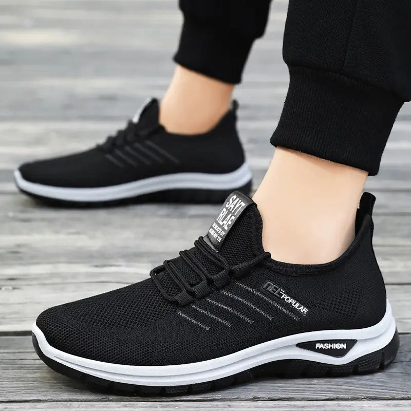 Black lightweight knit slip-on sneakers worn by a person, showcasing the engineered mesh upper, white midsole with black &