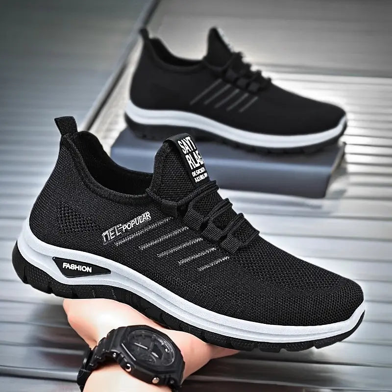 Black lightweight breathable knit sneakers with white midsole stripe and 'FASHION' text, held by a hand wearing a watch.