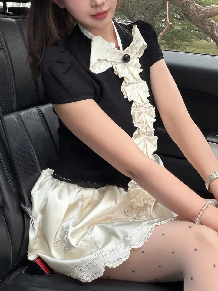 Woman wearing a black short sleeve knit top with cascading white ruffles and a black bow, seated in a car.