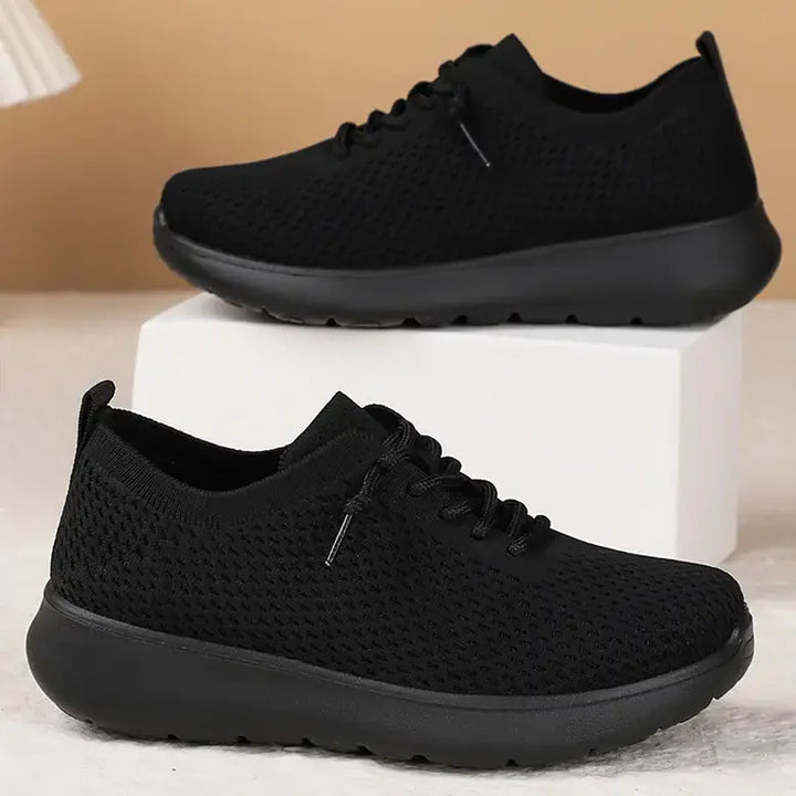 Two black breathable knit trainers are displayed stacked, featuring a seamless upper, lace-up closure, and a contrasting sculpted foam sole for everyday athleisure wear.