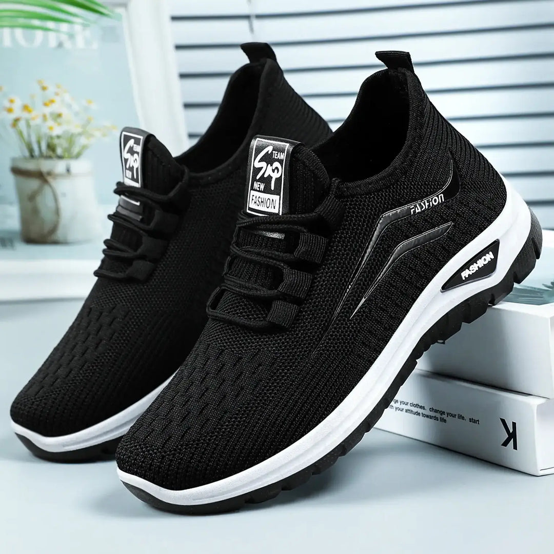 A pair of black breathable knit trainers shown from a three-quarter front view, featuring a white midsole, black outsole with &