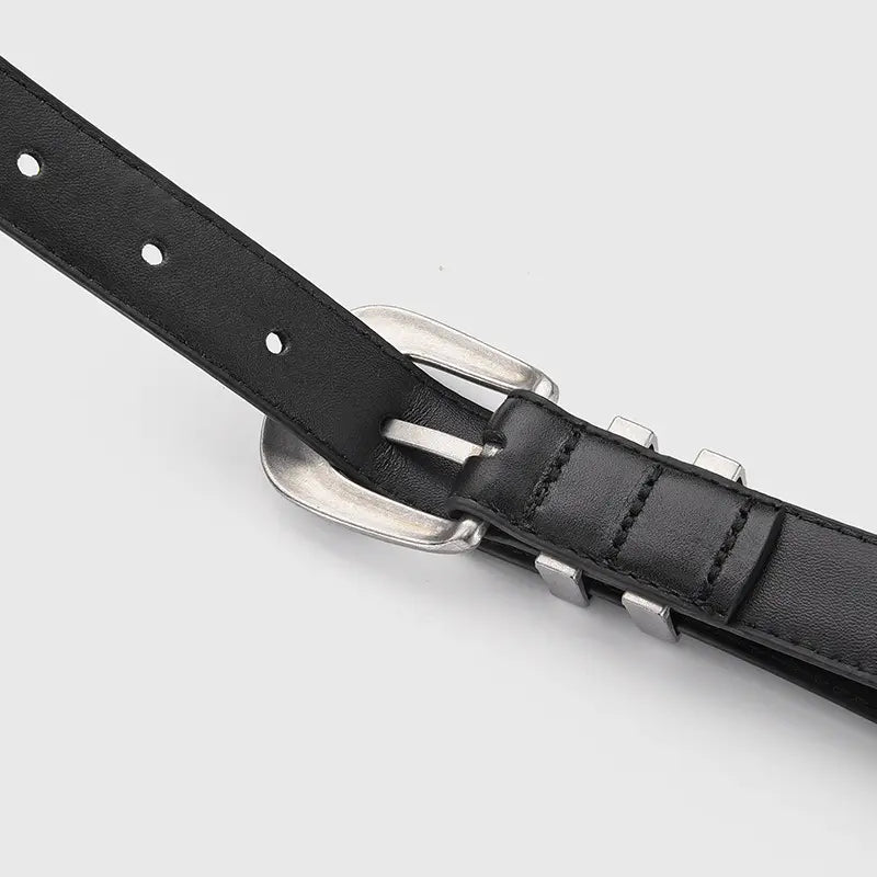 Close-up of a black genuine leather belt featuring an antiqued silver Western-style buckle and a dual slot metal keeper, showcasing detailed craftsmanship.