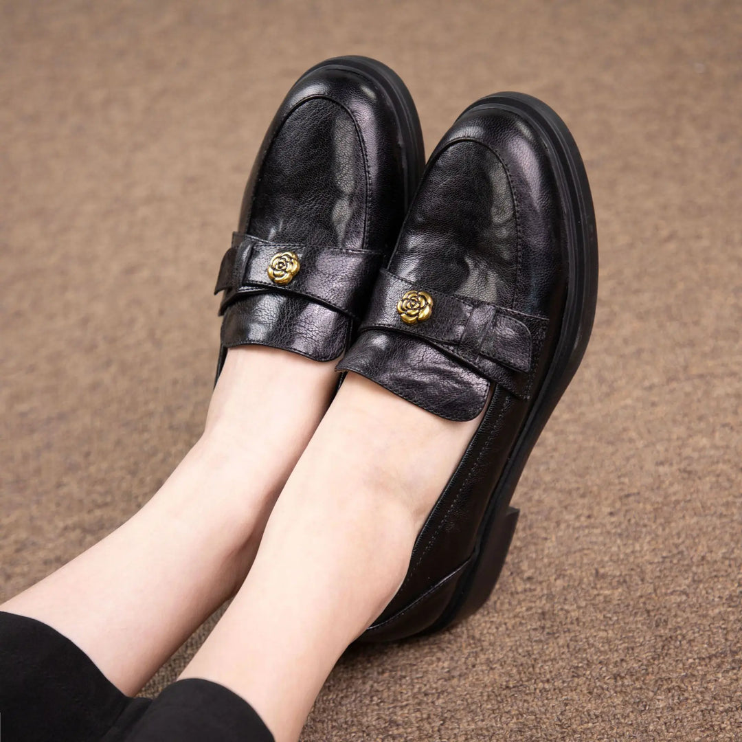 Pair of chic black sheepskin leather loafers with decorative floral buckle detail, worn on feet against a textured brown carpet background.