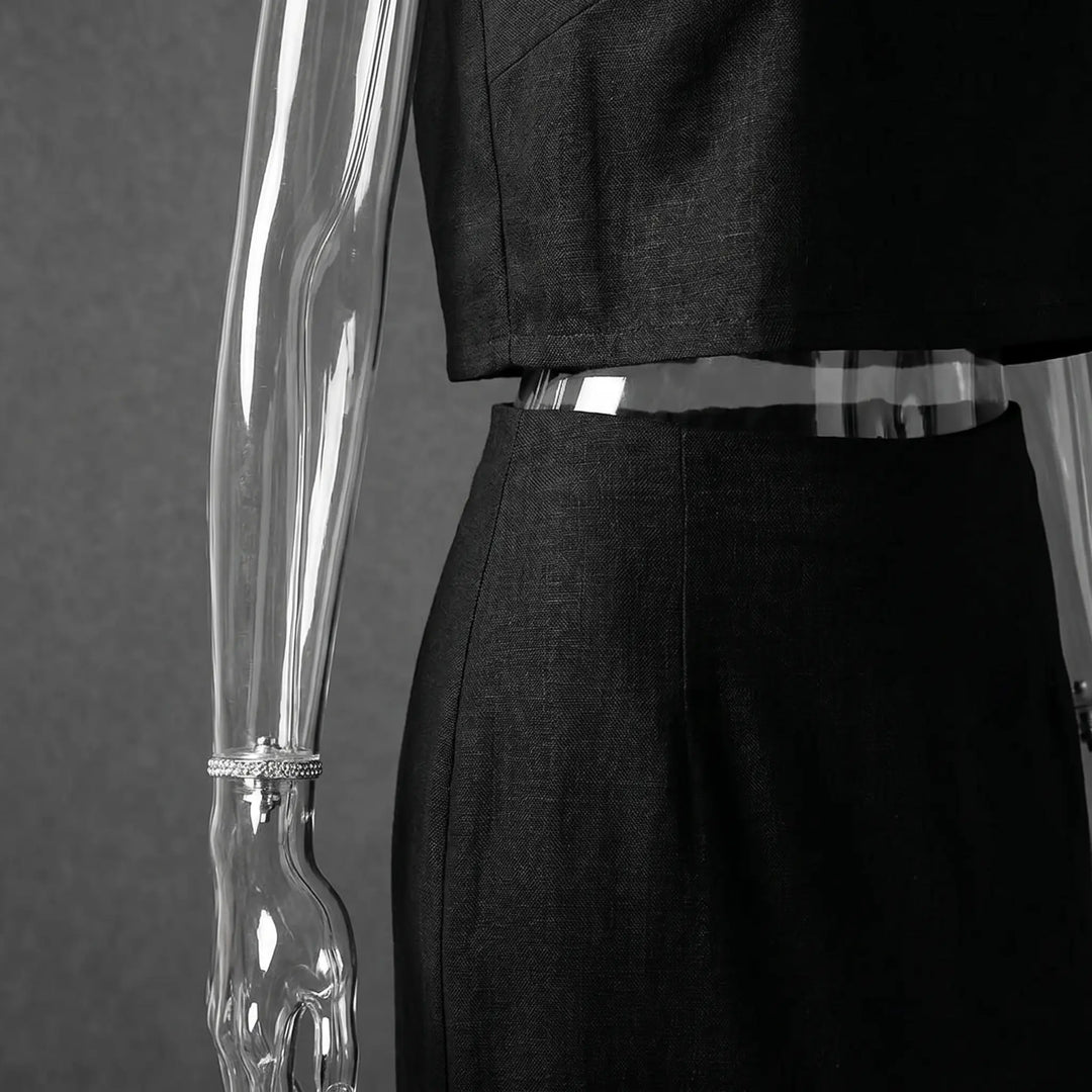Close-up of a black linen-blend sleeveless crop top and fitted midi skirt, showcasing the fabric texture and subtle shoulder padding detail on a mannequin.