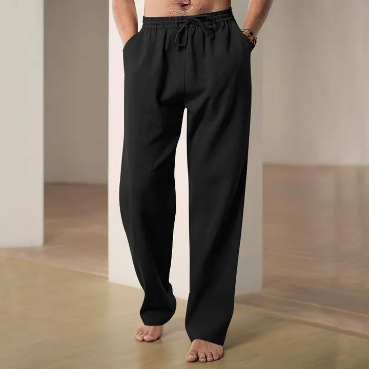 Man wearing black wide-leg linen-blend trousers with drawstring waist and side pockets, shown in a relaxed, casual indoor setting. Offers a comfortable and stylish look.