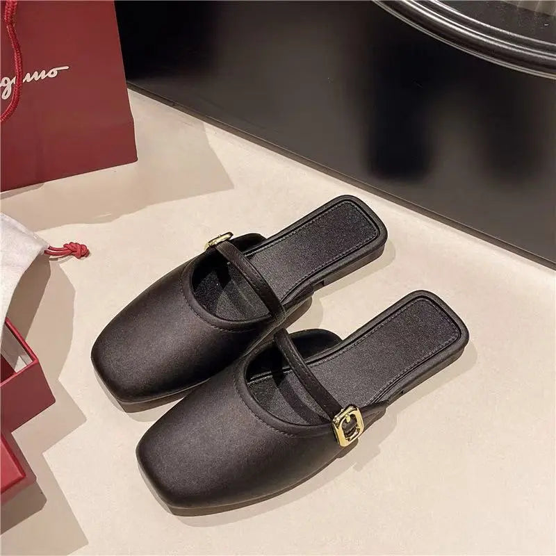 Black matte faux leather slip-on mules with square toes and a delicate gold-tone buckle strap across the vamp, presented in a flat-lay studio shot.