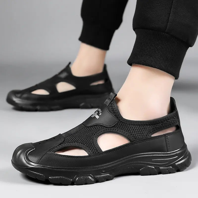 Men's black breathable mesh and synthetic leather sandals worn by a model, showcasing the slip-on design, open-toe cutouts, and rugged sole on a neutral studio background.