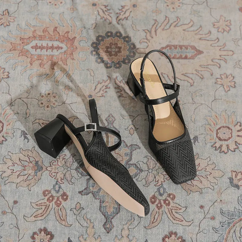 Black heeled slingback sandals with a square toe, woven mesh vamp, and adjustable slingback strap with a silver buckle, displayed flat lay on a vintage rug.