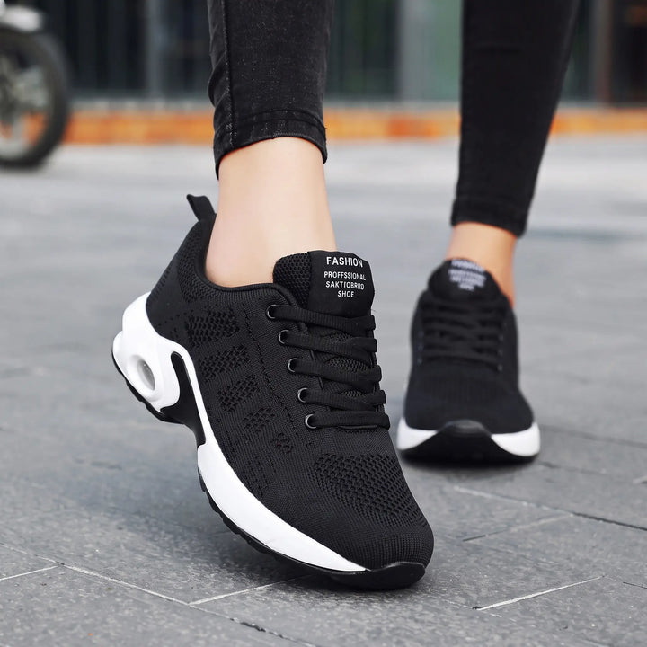 Black lightweight breathable mesh sneakers for women with a visible air cushion sole and lace-up closure, shown from a front angle in an outdoor setting.