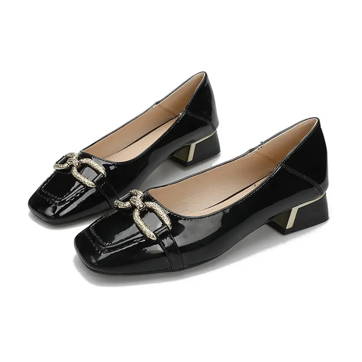 Elegant black patent leather square toe pumps adorned with a decorative gold-tone buckle and featuring a stylish block heel with a metallic gold cap.