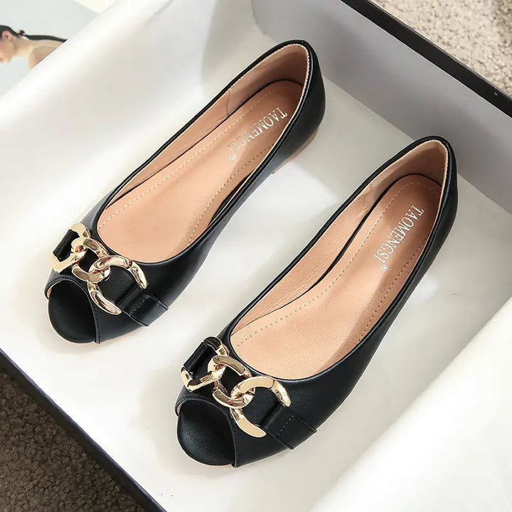 Black faux leather peep-toe flats adorned with a chic gold-tone chain embellishment and buckle, presented flat with a clean studio background.