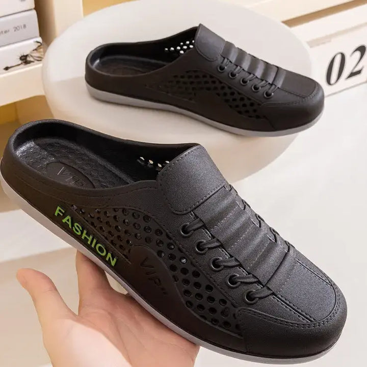 A pair of black breathable slip-on mule clogs with a perforated vamp and faux lace-up detail, viewed from a three-quarter angle on a studio shelf.