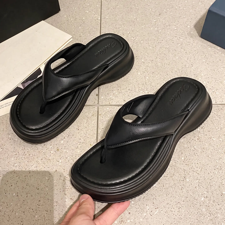 A pair of black Zethel platform thong sandals with thick EVA soles and wide synthetic straps, shown from a top-down angle on a tiled studio floor.