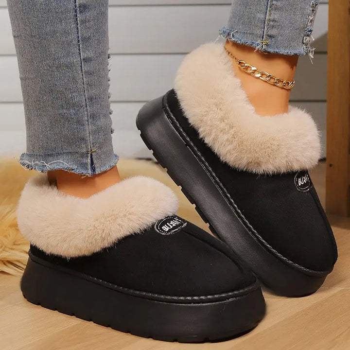 Black Vexel plush mule slippers with warm faux fur trim and a thick platform sole, worn with denim jeans on a home floor.